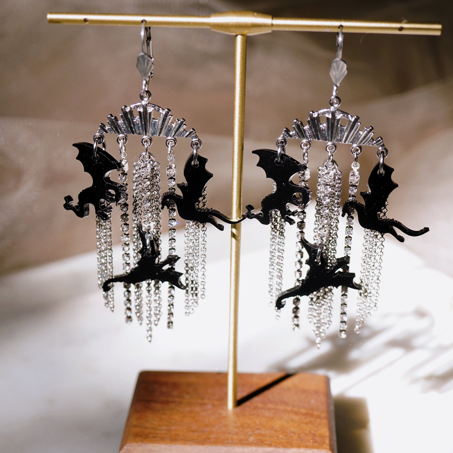 Pair of earrings with black dragon figures and crystal elements on a wooden stand.
