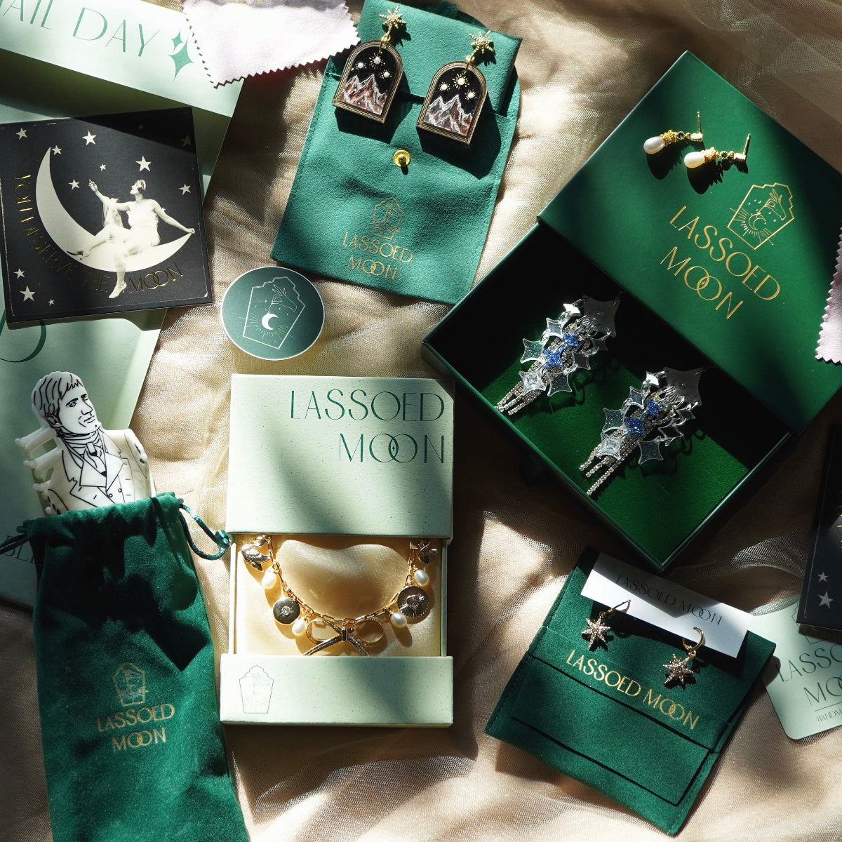 An above view of an arrangement of luxurious green jewelry packaging showing the logo Lassoed Moon with some jewelry pieces and hair accessories mixed throughout
