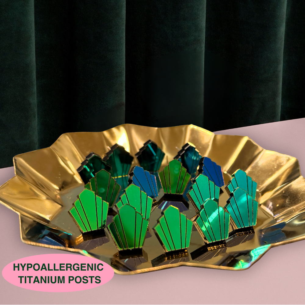 Decorative dish with green and blue geometric stud earrings on a gold base against a dark curtain background.